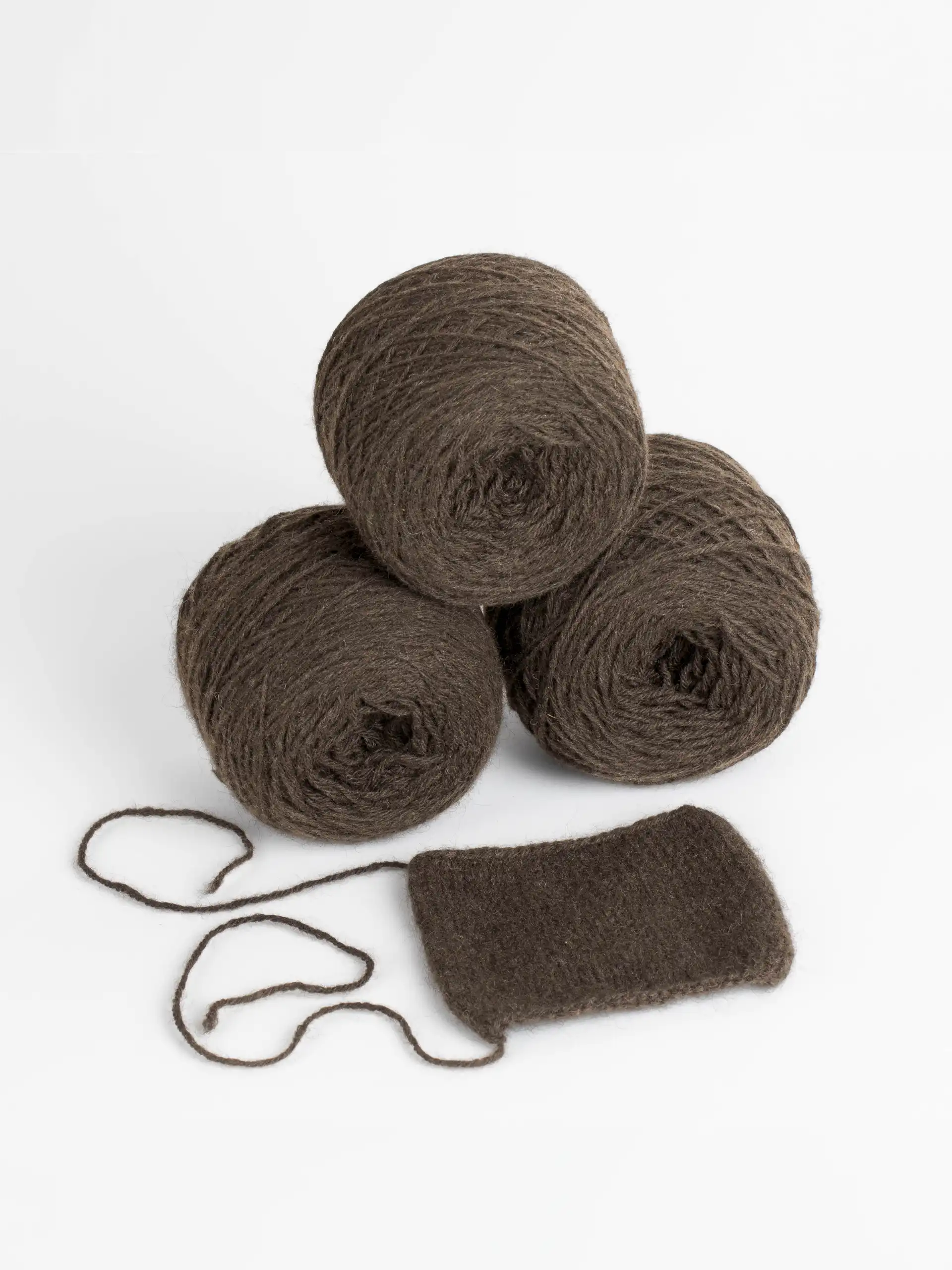Trois pelotes de laine de yack brun foncé empilées sur un fond blanc avec un échantillon de tricot rectangulaire et un fil détaché.