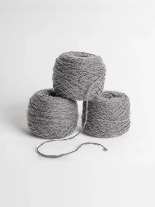 Quatre pelotes de laine de yack grises empilées sur un fond blanc, évoquant la douceur et la chaleur naturelle.