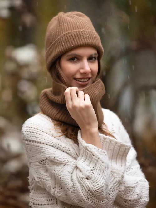 Cette image montre une femme adulte portant un tour de cou camel assorti à un bonnet. Le tour de cou, tricoté en laine de chameau 100 % mongol, offre une chaleur luxueuse et un confort optimal. Idéal pour les hivers rigoureux, ce chauffe-cou est un accessoire élégant pour homme et femme. Découvrez la qualité exceptionnelle de la laine de chameau avec