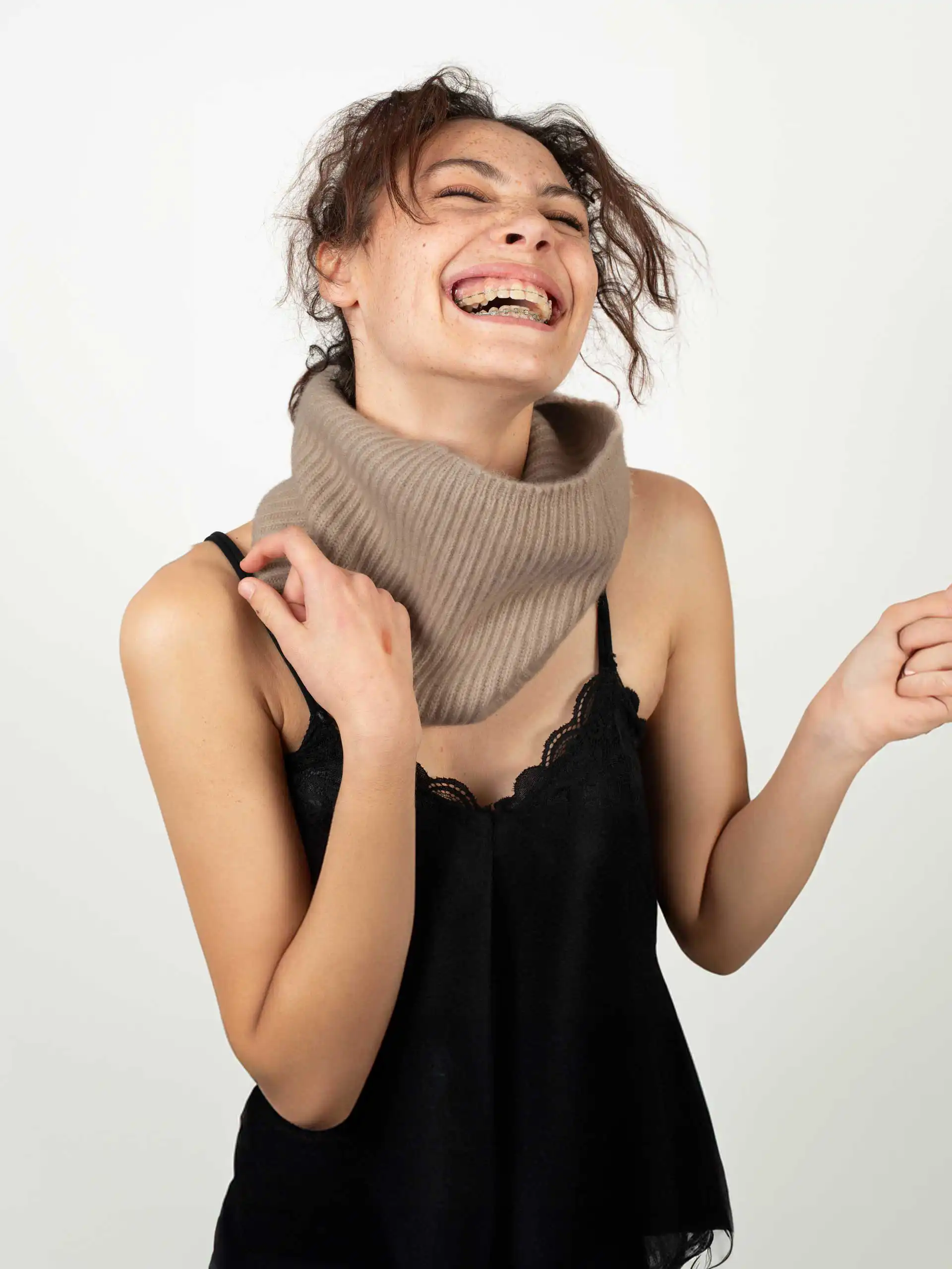 Une femme souriante portant un tour de cou en cachemire beige et un haut noir, illustrant l'élégance et la chaleur du produit.