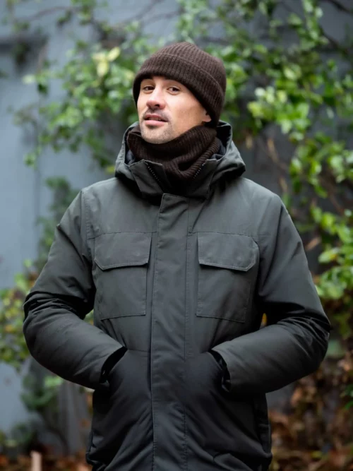 Un homme portant un tour de cou en yack marron et un bonnet assorti, se tient dehors en hiver. Le tour de cou est fait de laine 100% mongole.