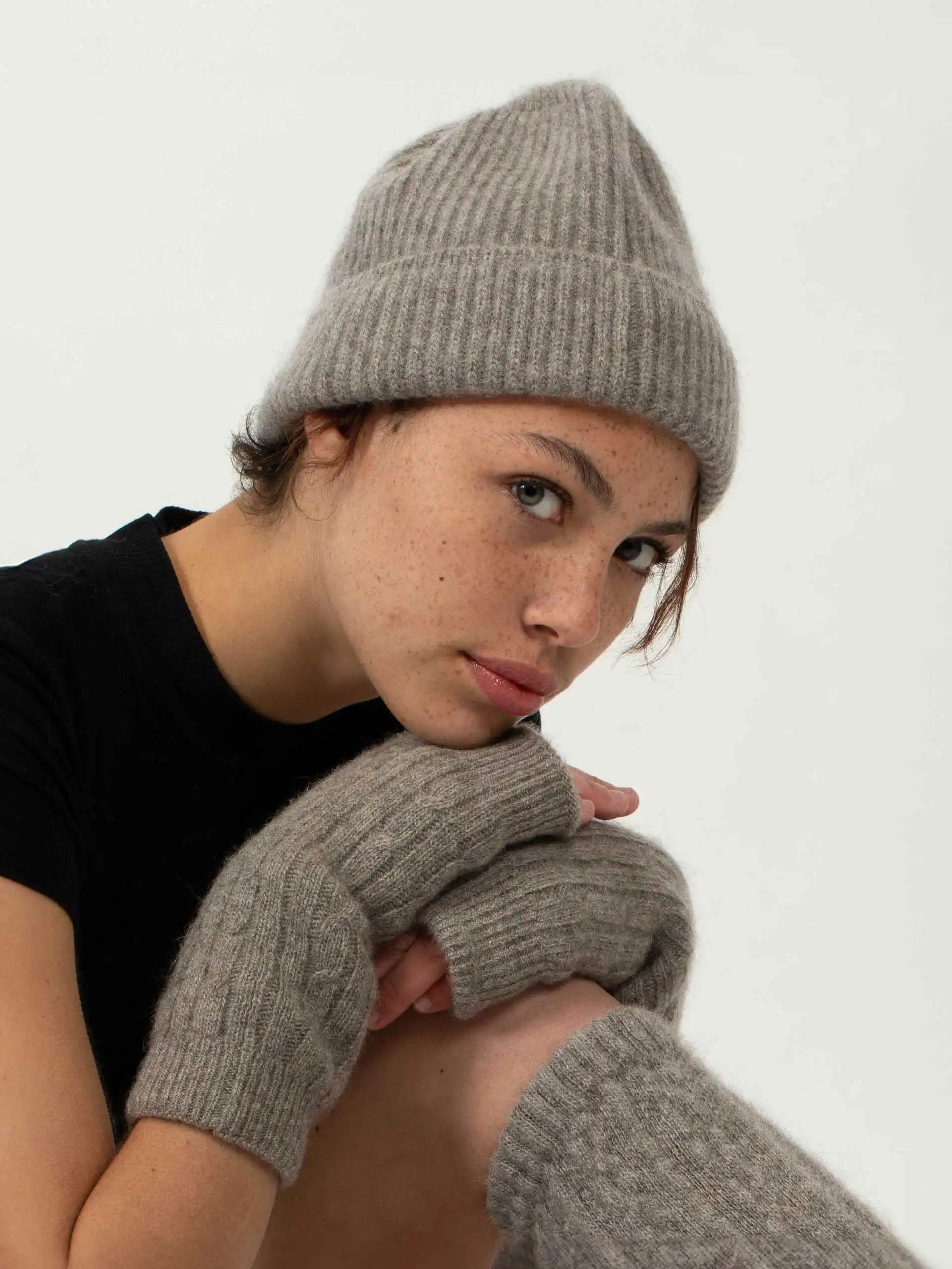 Jeune femme aux taches de rousseur portant un BONNET YACK Gris cendré et des mitaines assorties, regard intense vers la caméra