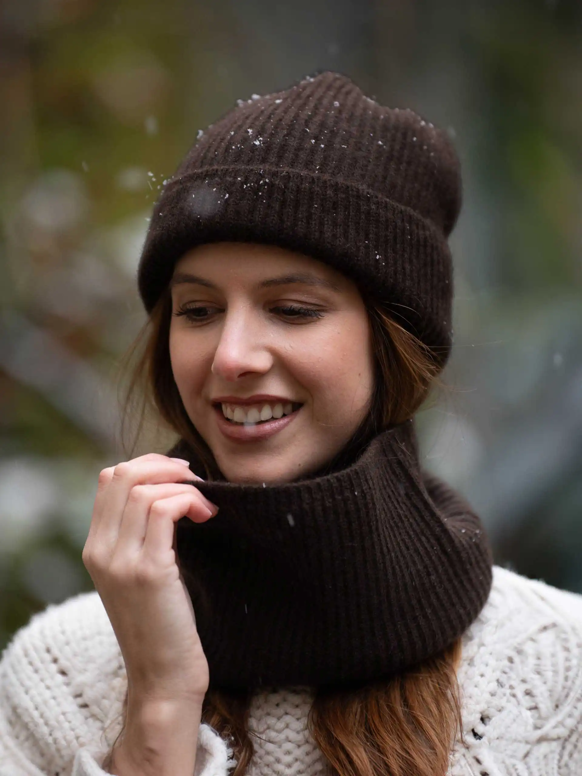 Femme souriante portant un BONNET YACK Marron foncé et une écharpe assortie sous la neige