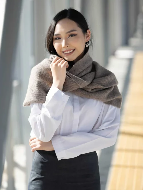 Femme souriante portant un SNOOD YACK gris autour des épaules, ajoutant une touche d'élégance à sa tenue hivernale.