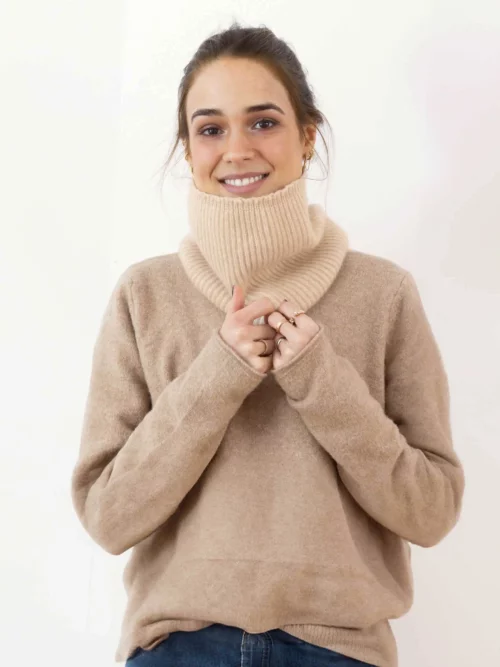 Jeune femme souriante portant un tour de cou en cachemire beige, tricoté pour offrir chaleur et élégance. Parfait pour les journées froides d'hiver.