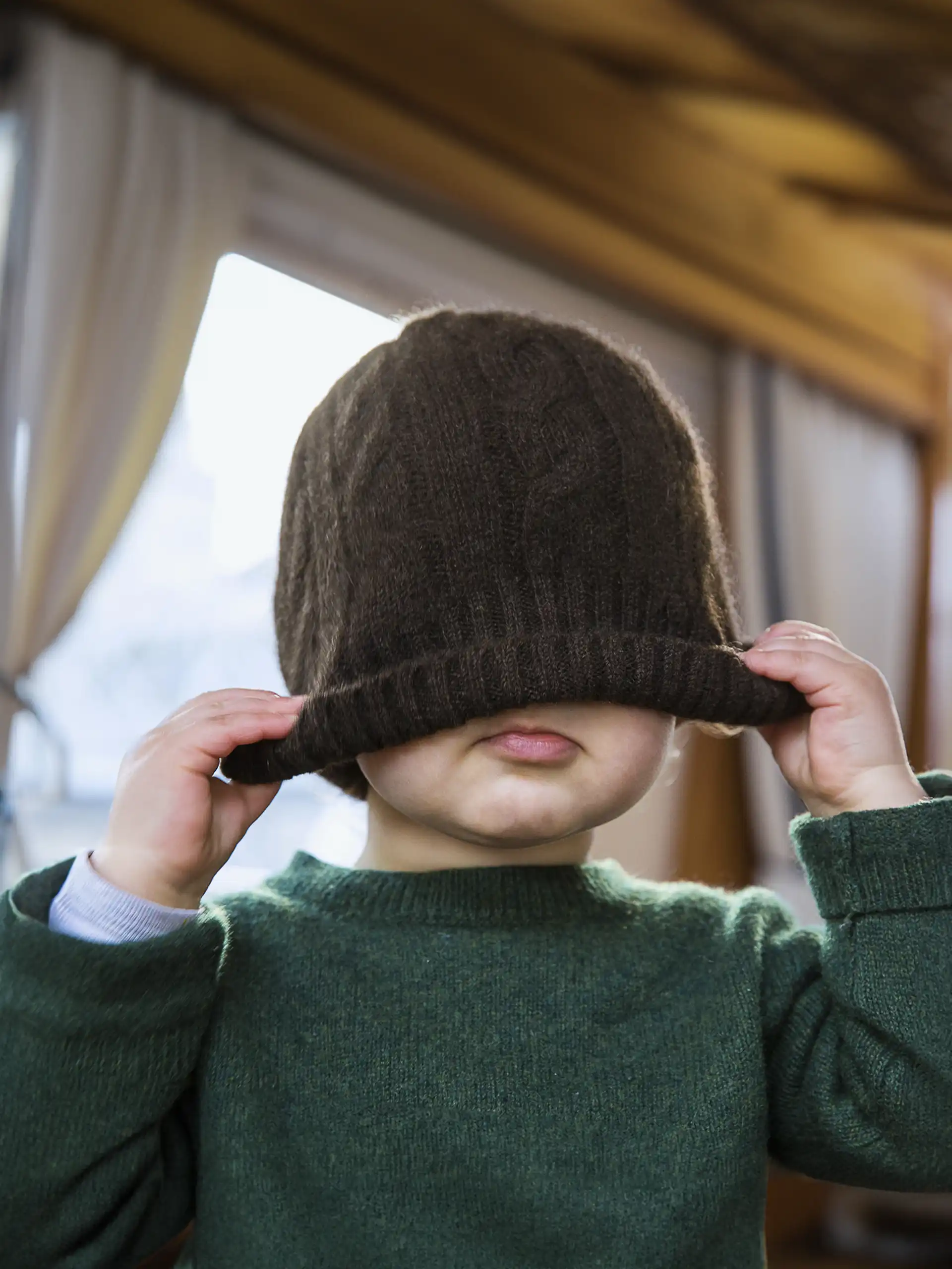 Un enfant portant un bonnet yack marron foncé torsadé de Mongolie, ajustant le bonnet sur sa tête.