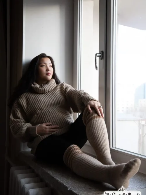 Femme regardant par la fenêtre tout en portant des chaussettes mouton longue crème