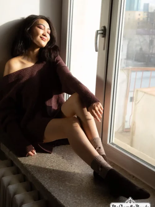 Femme portant des chaussettes rennes marron foncé en se relaxant près de la fenêtre.