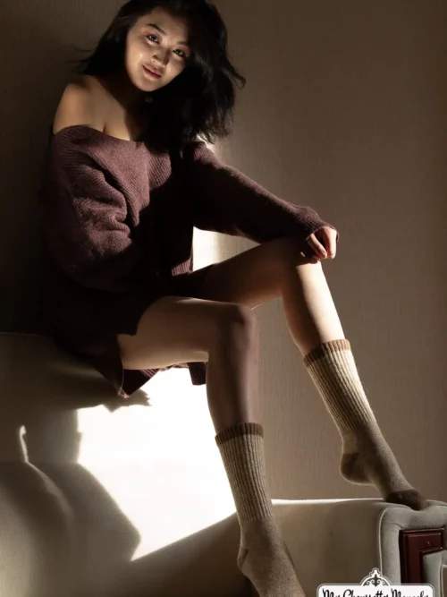 Femme en pull marron assise, mettant en valeur ses chaussettes mouton crème