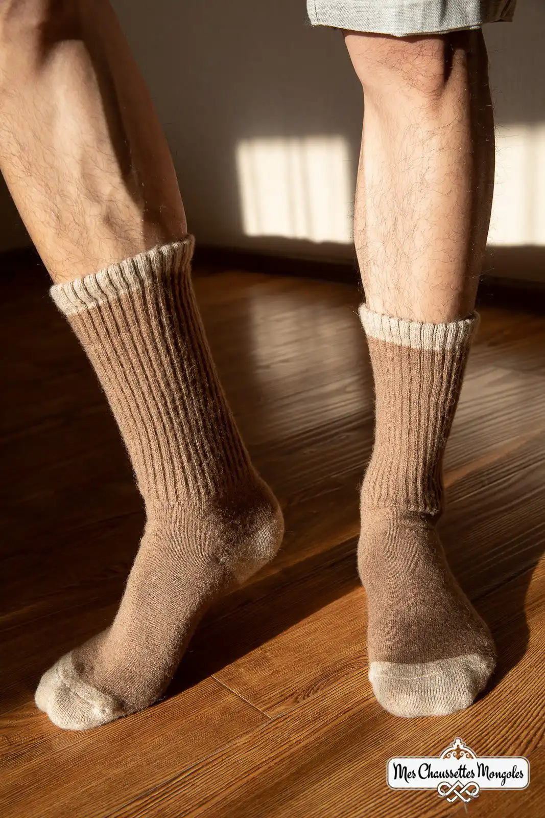 Homme en short portant des chaussettes hautes marron clair sur un sol en bois