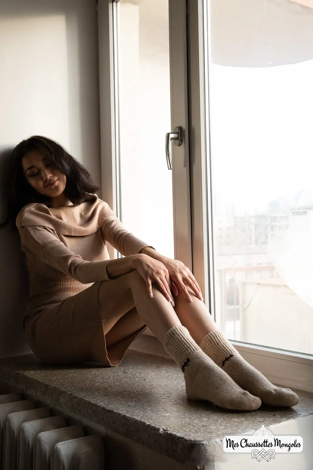 Femme assise près d'une fenêtre ensoleillée portant des chaussettes motif chameau