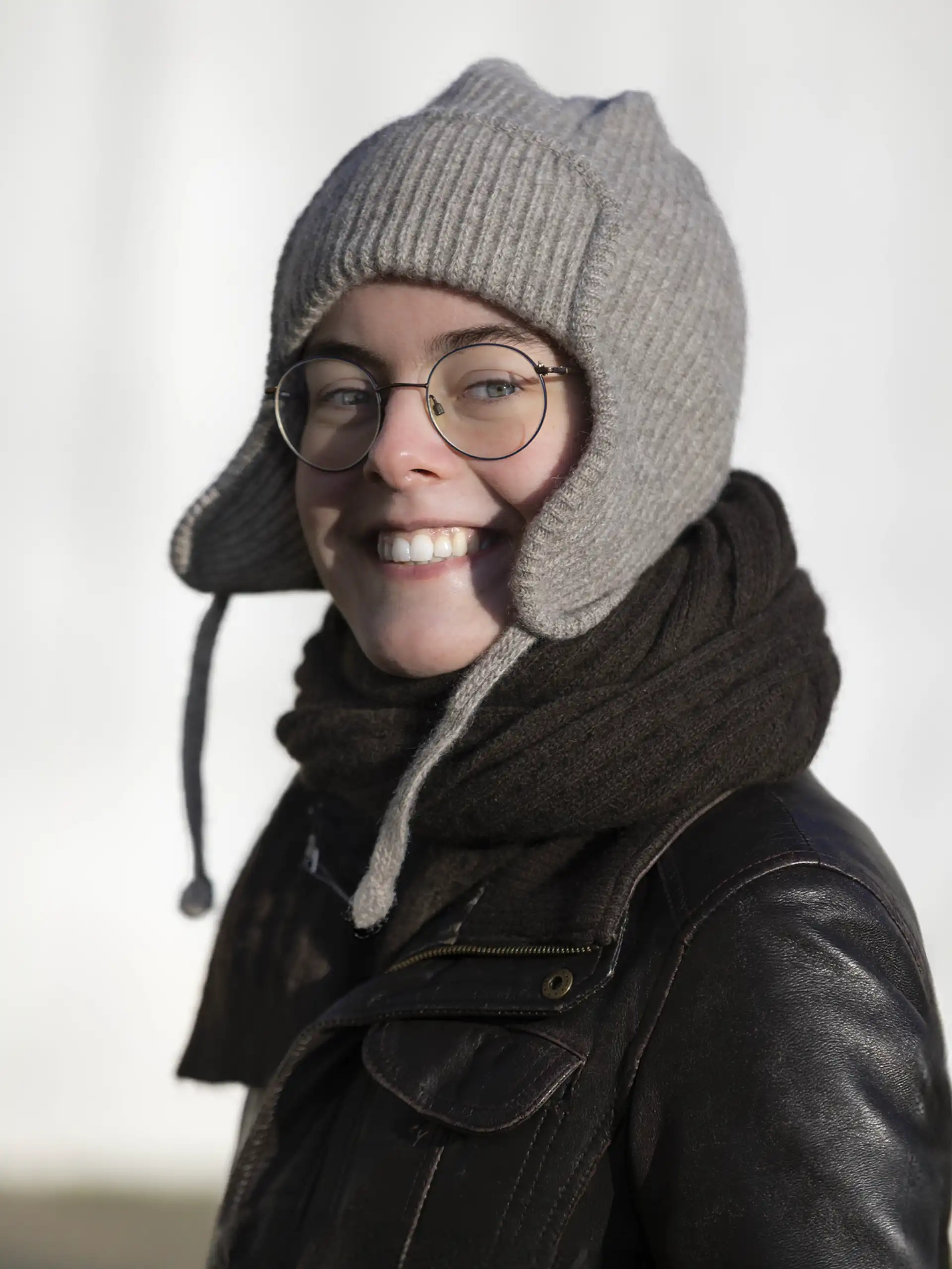 Femme souriante portant une chapka gris en laine avec des lunettes et une écharpe noire